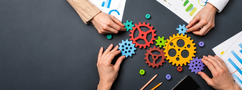 Hands assembling colourful gears on a desk — collaboration across operations